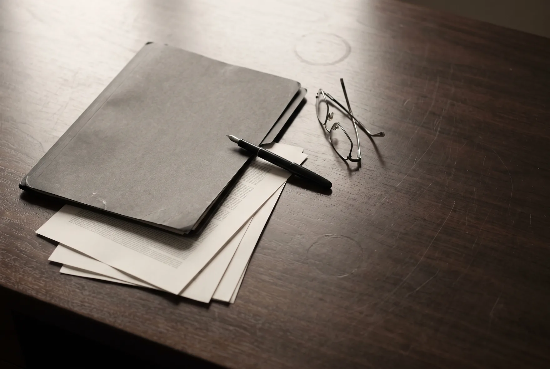 An executive desk in Hong Kong with a board pack, a fountain pen and reading glasses, the material an AI programme session begins from.